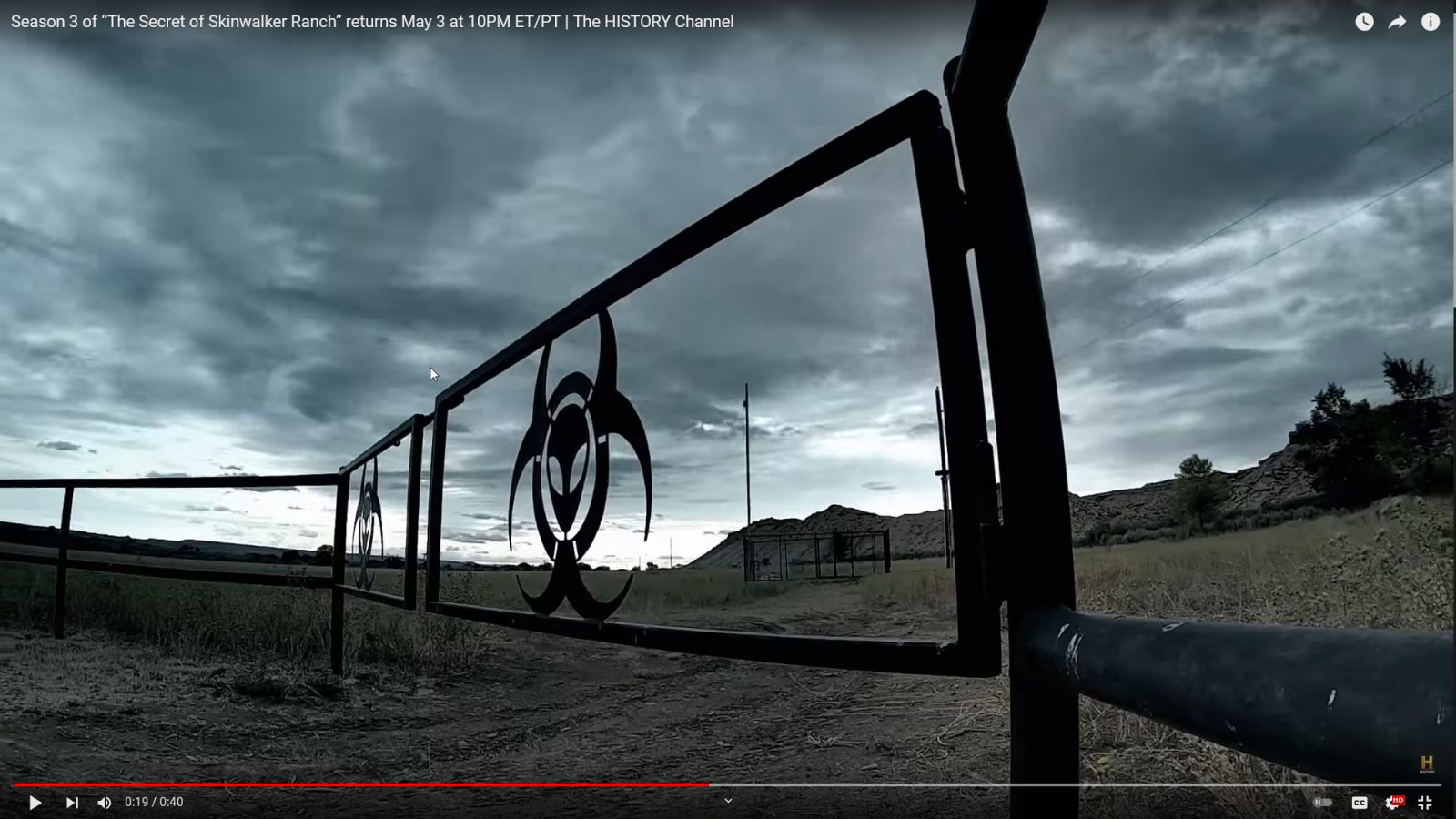 Teaser Screencap showing the powerlines viewed through a gate with the Skinwalker ranch logo, with the mesa in the background.